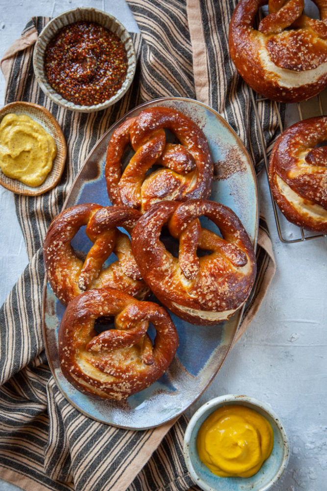 Sourdough pretzels on a plate surrounded by small bowls of mustard.
