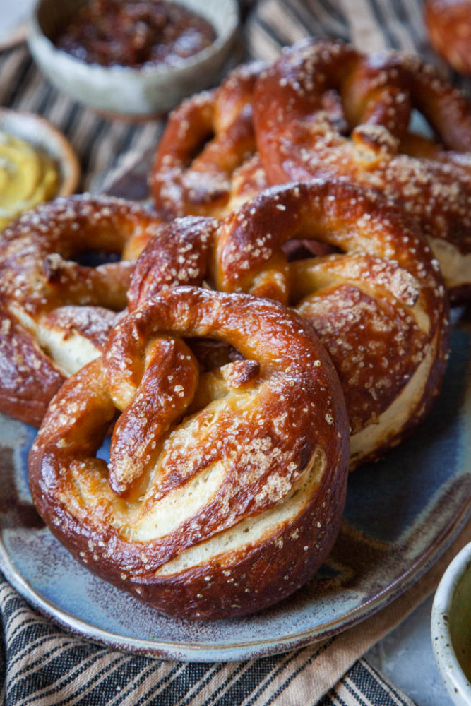 Sourdough soft pretzels on a plate with small bowls of mustards next to it.