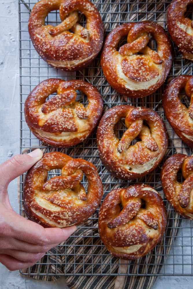 a hand reaching for a handmade sourdough soft pretzel on a cooling rack.