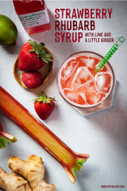 a glass of strawberry rhubarb soda made with homemade syrup surrounded by strawberries, rhubarbs, ginger and lime.