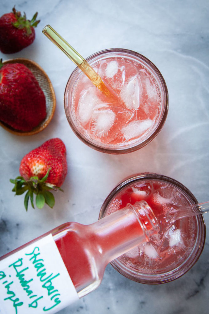 a bottle of strawberry rhubarb syrup being poured in a glass of sparkling water.