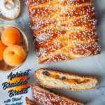 A loaf of braided apricot yeast bread with dried blueberries on a marble surface with a couple of apricots next to it.