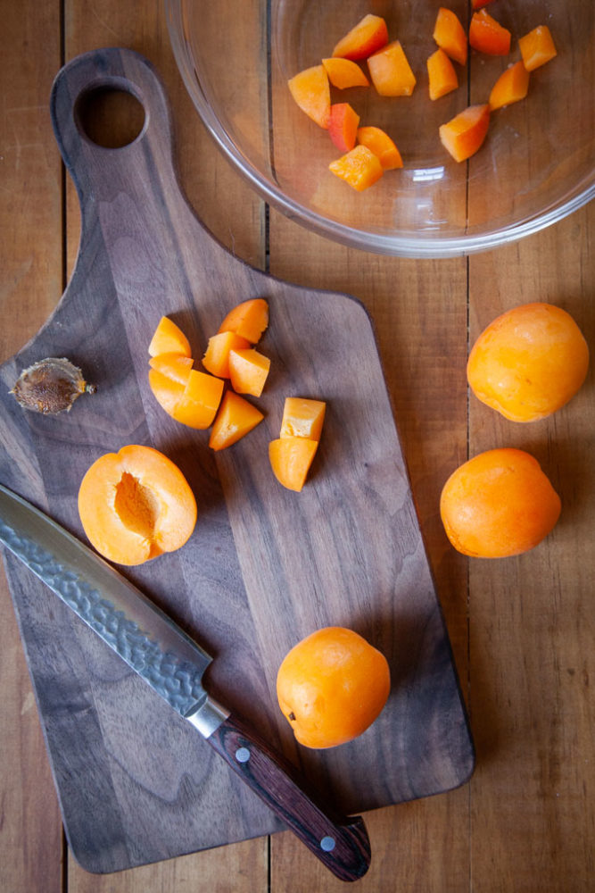 A cutting board with fresh apricots being cut on it.