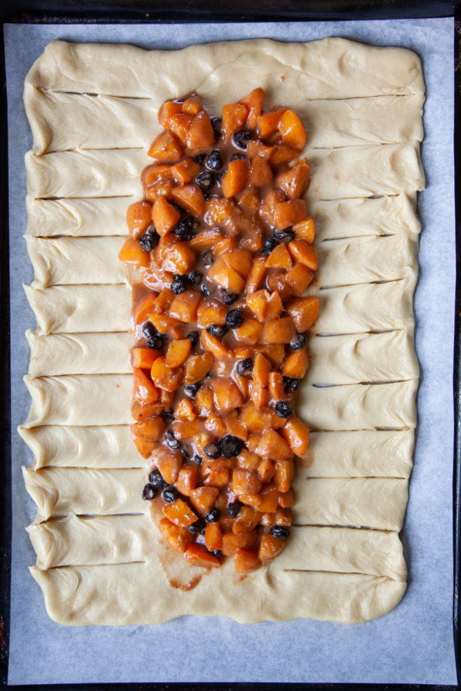 Apricot blueberry filling on top of a rectangle of bread dough cut into strips.