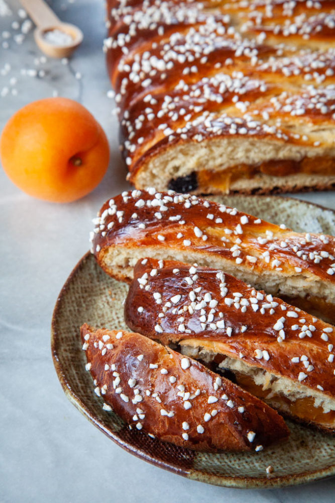 Apricot yeast bread sliced on a plate, with an apricot in the background.