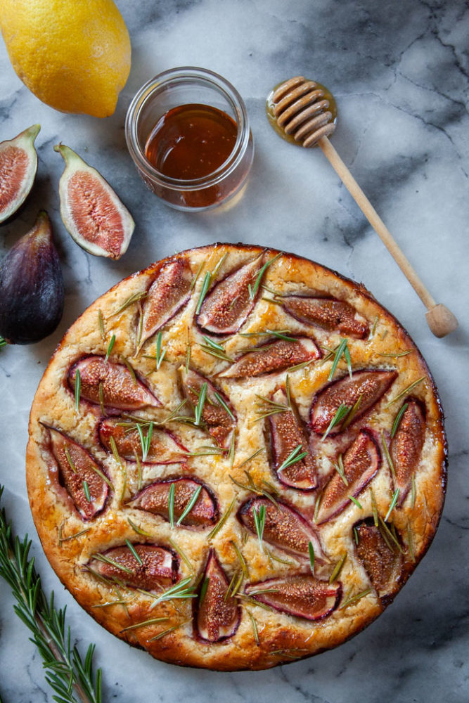 fig rosemary focaccia on a marble surface surrounded by ingredients for the dish.