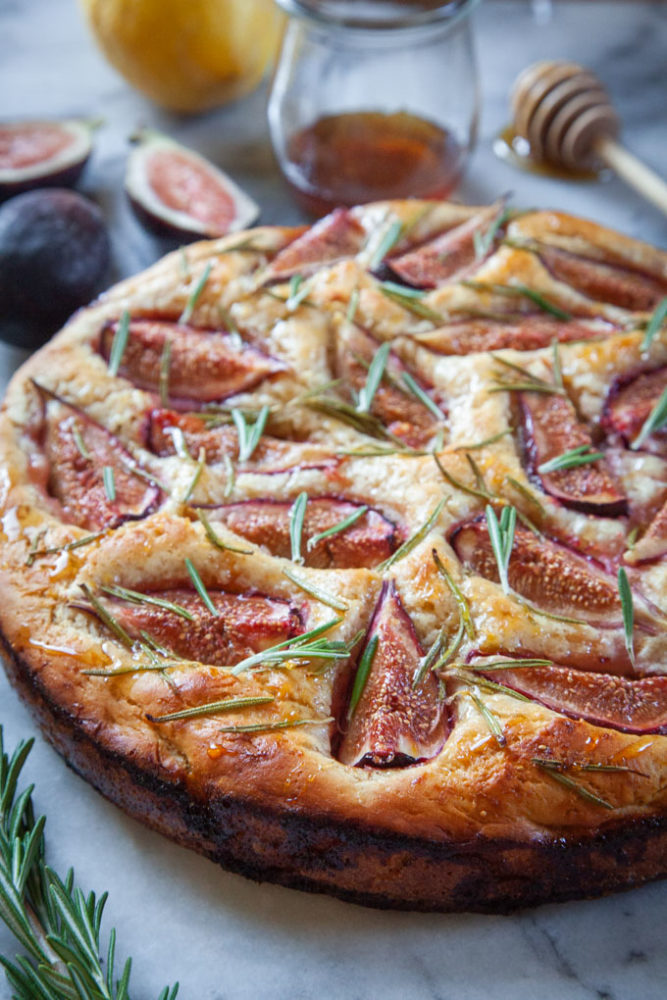 fig rosemary focaccia on a marble surface surrounded by ingredients for the dish.