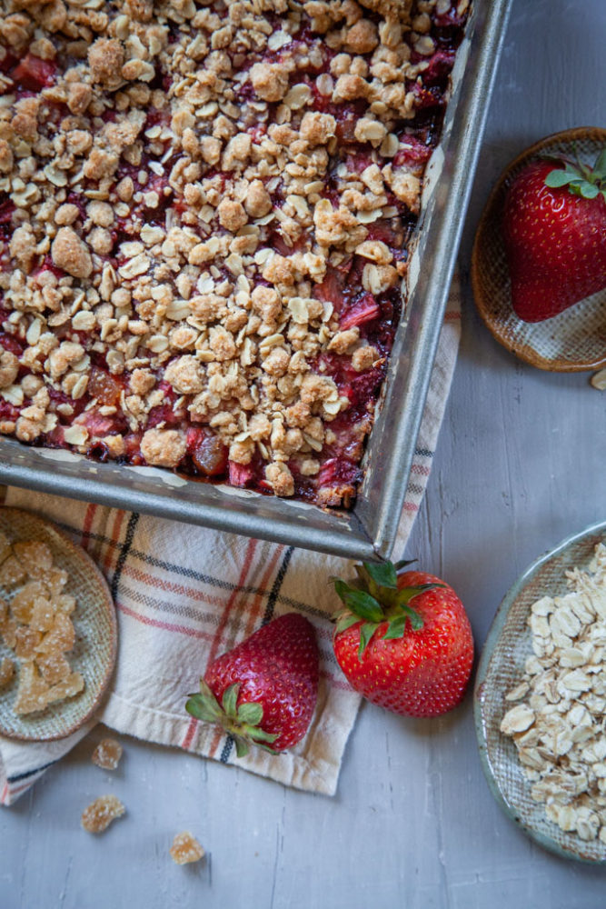 a pan with with strawberry oatmeal bars in it, surrounded by oats and strawberries.
