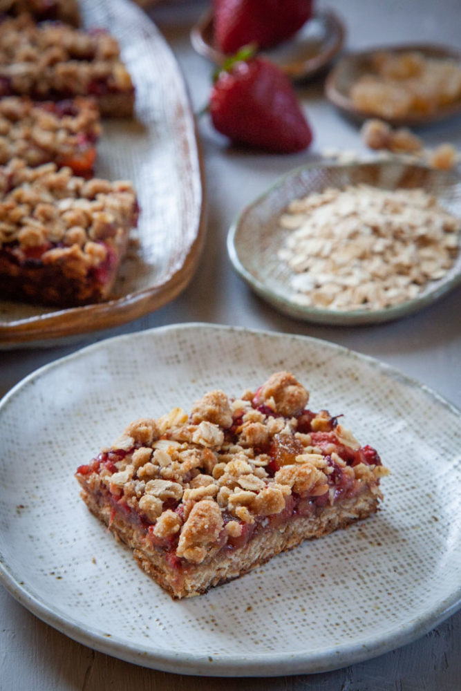 a single strawberry oatmeal bar on a plate, with more bars behind it.