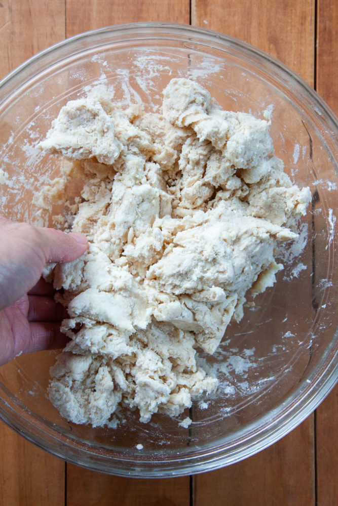 A hand mixing ingredients for a pie crust in a glass bowl.
