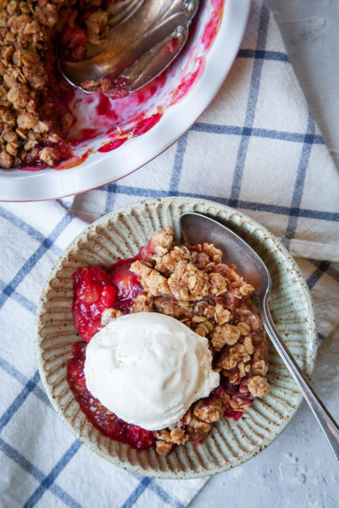 A serving of plum crisp with a scoop of vanilla ice cream on top.