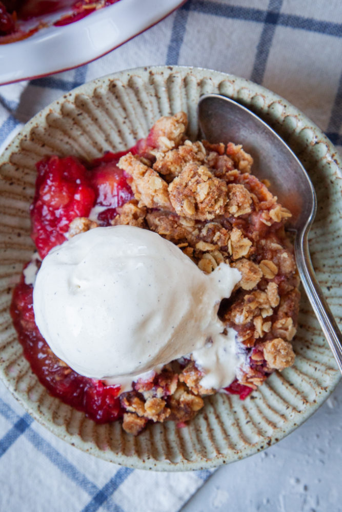 a bowl of plum crisp with vanilla ice cream on top.