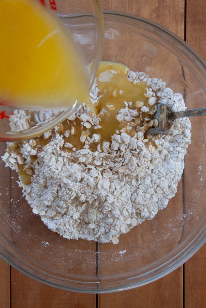 Drizzling melted butter into a bowl of crisp topping ingredients.