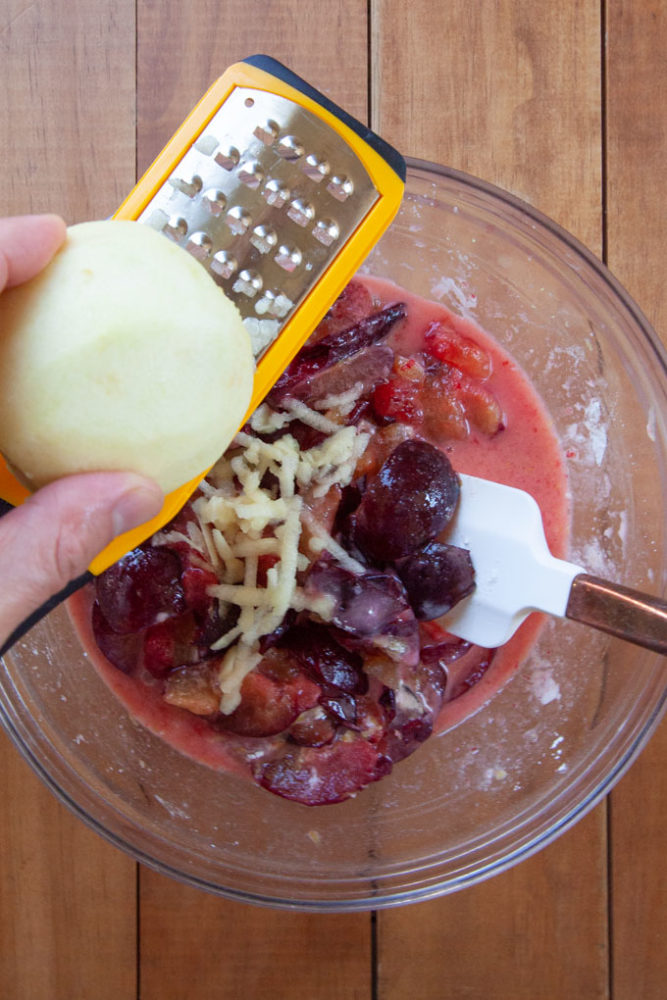 Grating an apple into a bowl of plum crisp filling.