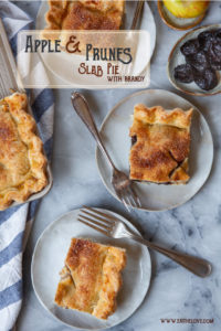 Slices of apple slab pie with prunes and brandy on plates, with a small plate of prunes and an apple next to them.