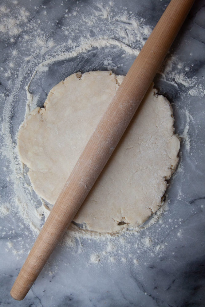 A rolling pin on top of a disk of pie crust dough.