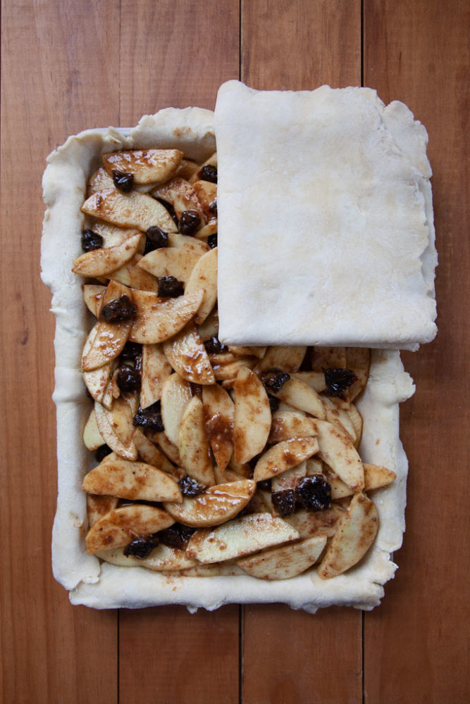 an apple and prunes slab pie being covered with the top pie crust.