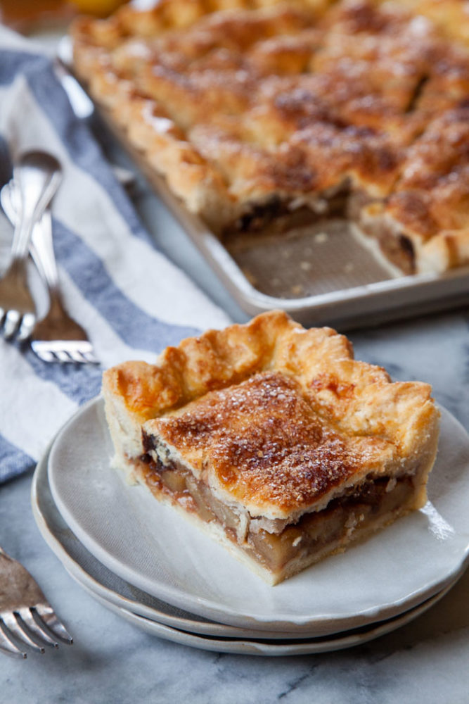 A corner slice of the apple and prunes slab pie on a plate, with the remaining pie behind it.