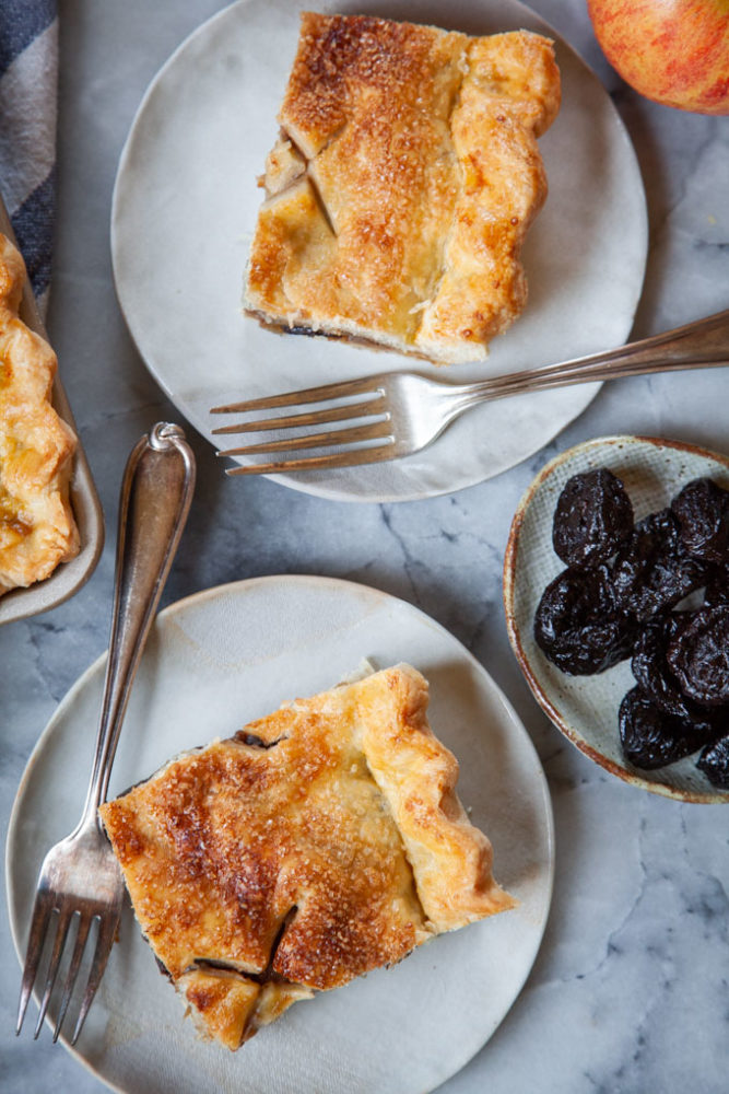 Apple and prune slab pie pieces on plates, with a small plate of prunes next to them.