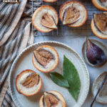 Fig financiers on a plate and wire cooling rack, surrounded by bay leaves, fresh figs and vanilla bean pod.