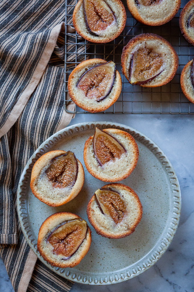 Fig financiers on a plate, next to more fig financiers on a wire cooling rack.