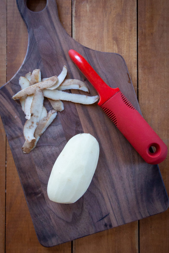 A small russet potato peeled on a cutting board.