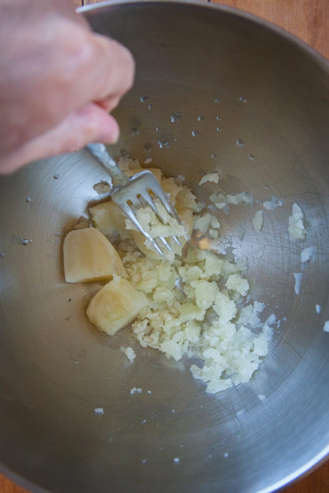 Mashing potato in a metal bowl with a fork.