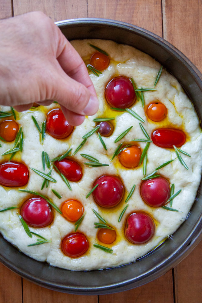 Sprinkling fresh rosemary leaves over the unbaked focaccia.