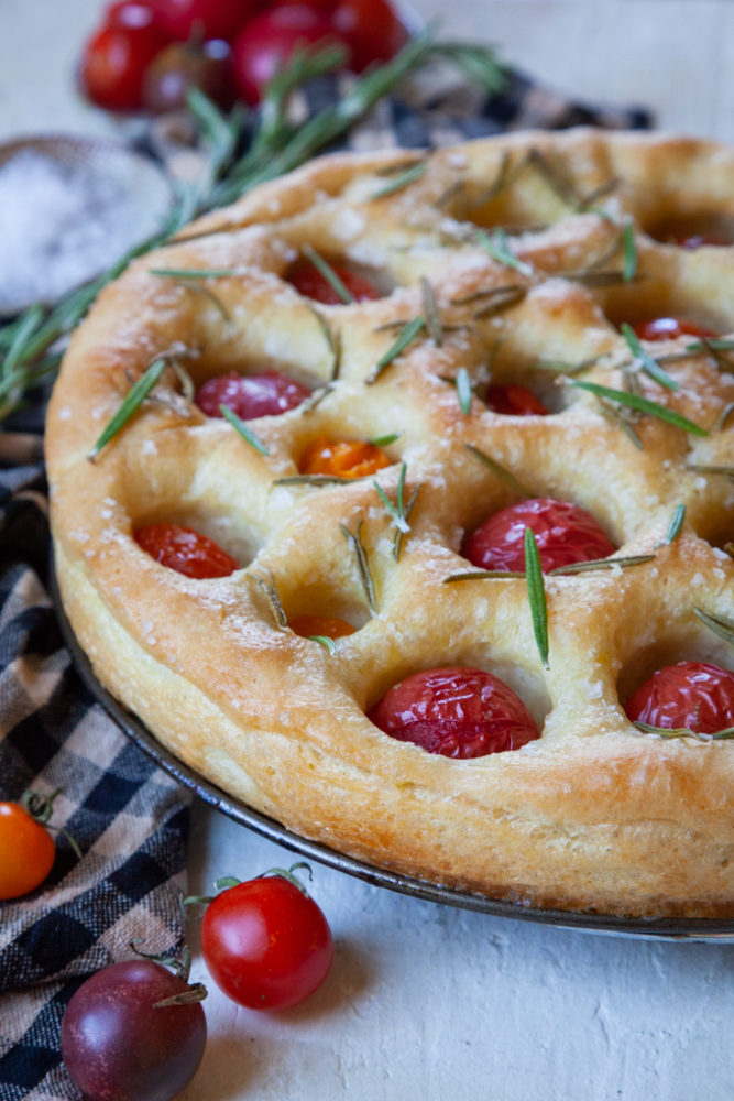 Tomato and rosemary focaccia on a table next to some cherry tomatoes