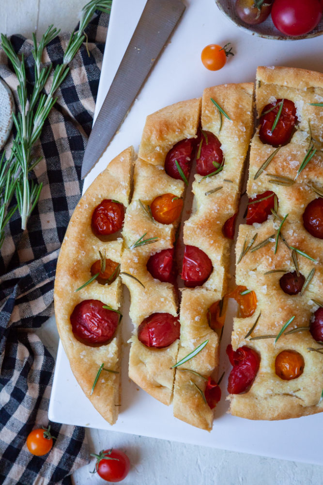 Sliced cherry tomato and rosemary focaccia on a white serving plate.