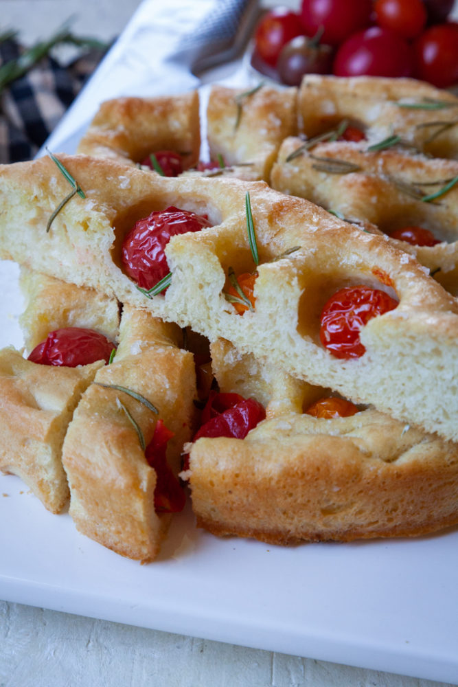 Sliced cherry tomato and rosemary focaccia on a white flat plate.