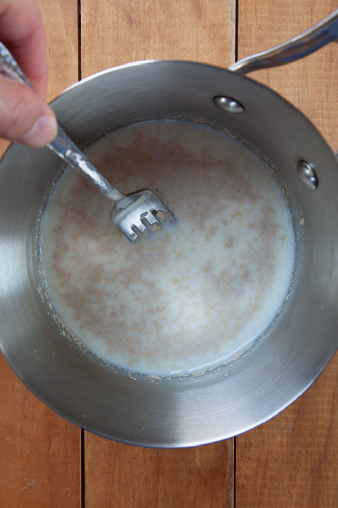 a fork stirring yeast into warm milk in a small pan.
