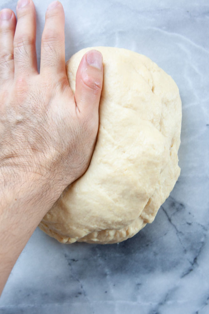 a hand kneading the cinnamon roll dough when it is nearly done being kneaded.