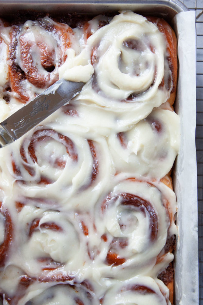 An offset spatula frosting cinnamon rolls with cream cheese frosting.