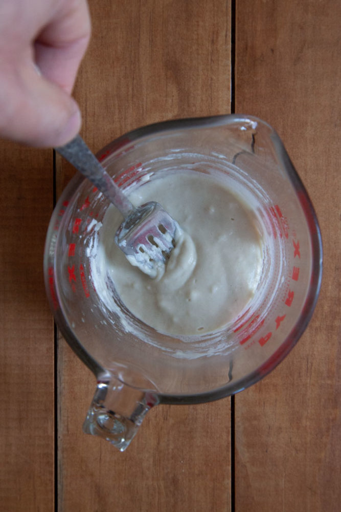 Pre-ferment dough being stirred together in a glass measuring cup with a fork.