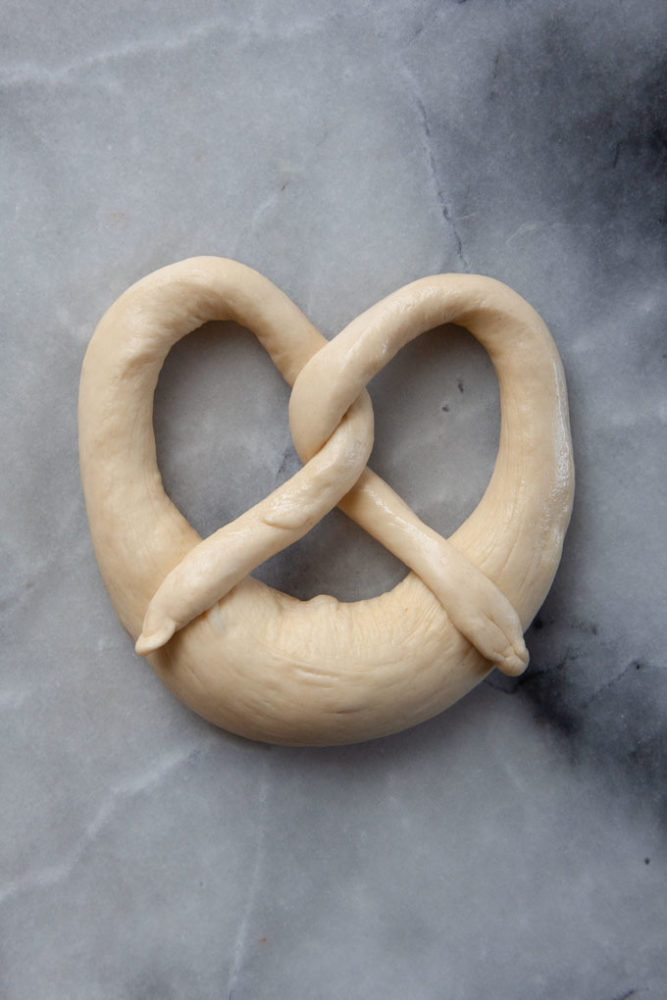 An unbaked formed pretzel on a marble surface.