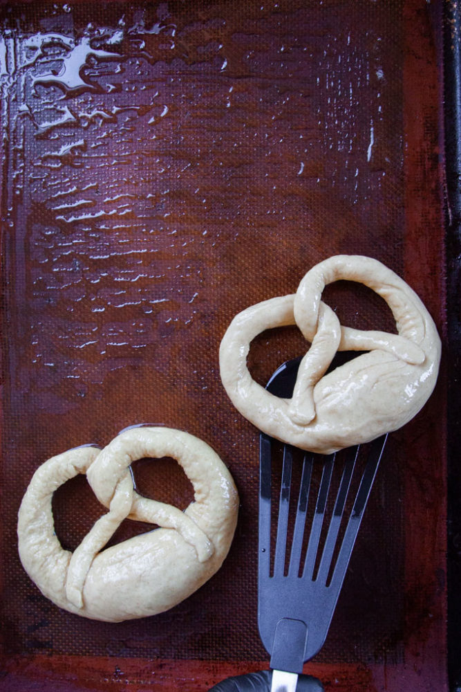 German pretzels dipped in lye, being placed on an oiled silicon baking mat.