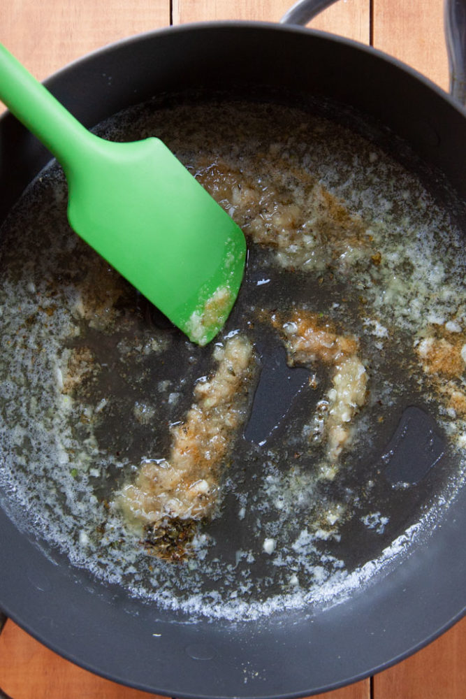 A green spatula cooking butter, garlic, oregano and salt in a pan.