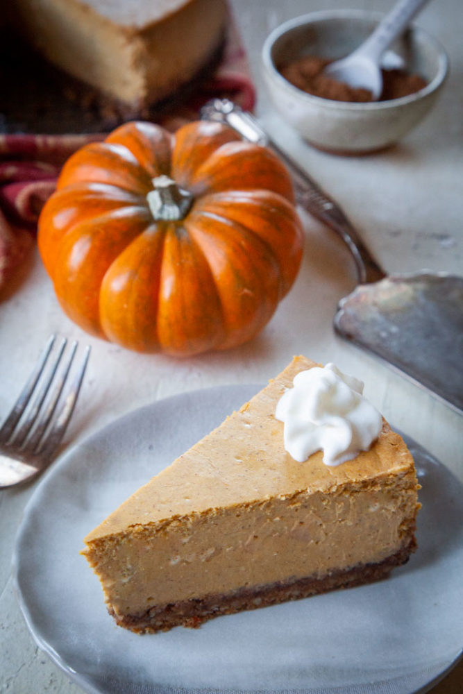 A slice of pumpkin cheesecake with whipped cream on it and the remaining cheesecake in the back.