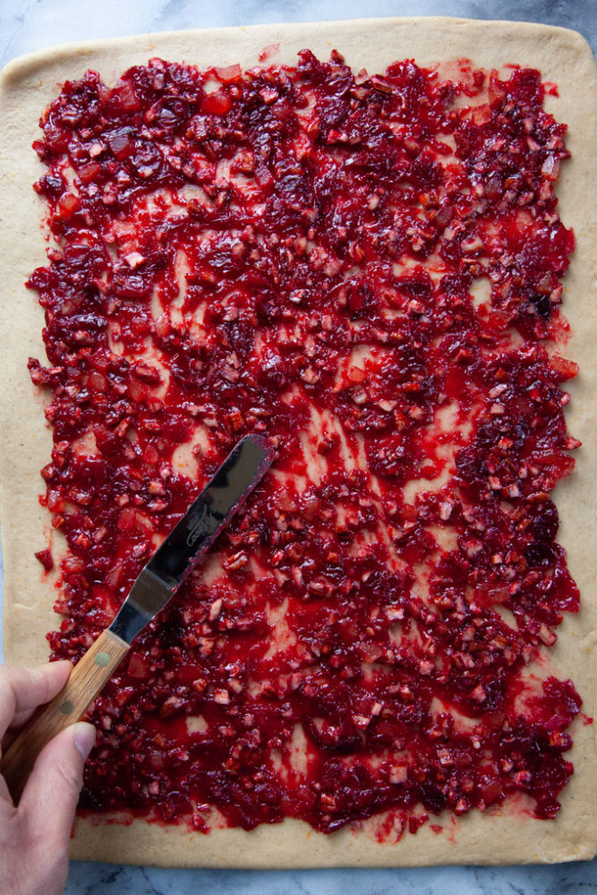 An offset spatula spreading the cranberry filing over the dough for the spiral bread.