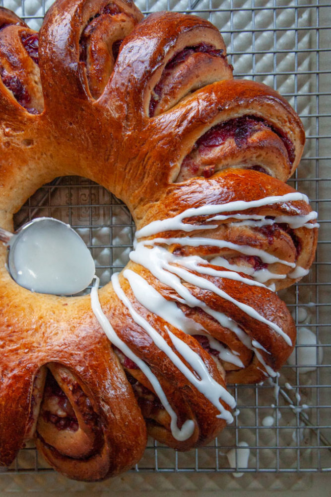 A spoon drizzling glaze over the cranberry swirl bread.