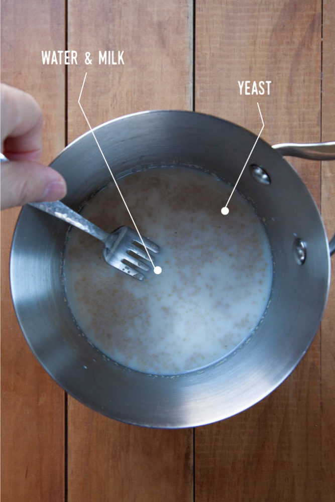 A pan with a fork stirring together warm milk, water and yeast.