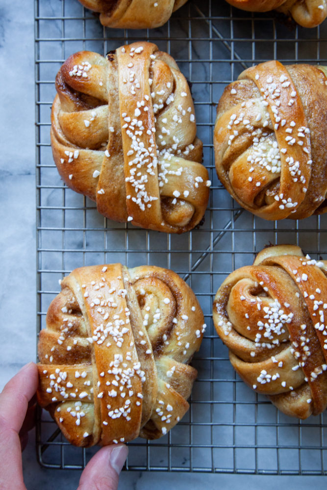 A hand reaching for a cardamom bun on a wire cooling rack.