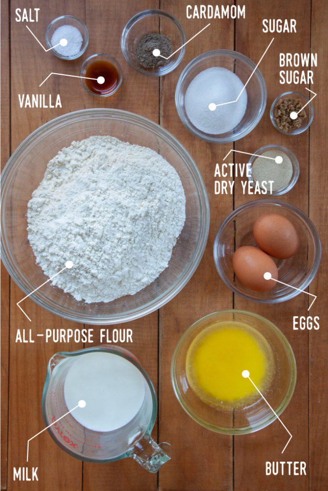 A photo with all the ingredients for the cardamom bun dough, including flour, milk butter, eggs, yeast, sugar, brown sugar, cardamom, vanilla and salt all in different bowls.