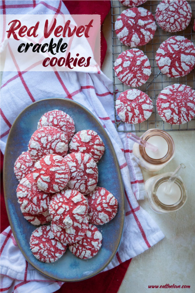 Red velvet crackle cookies on a blue plate, with two small milk bottles with milk in them next to it. Next to the milk bottles is a wire cooling rack with more cookies on it.