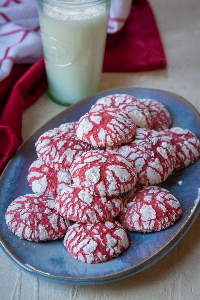 Red velvet crackle cookies on a blue plate with a glass of milk behind it.