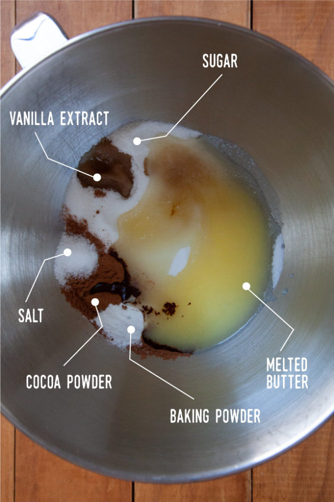 A metal bowl with sugar, melted butter, cocoa powder, salt, and baking powder in it.