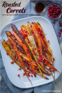 Roasted rainbow carrots with za'atar spices and drizzled with pomegranate molasses and seeds on a white serving plate.