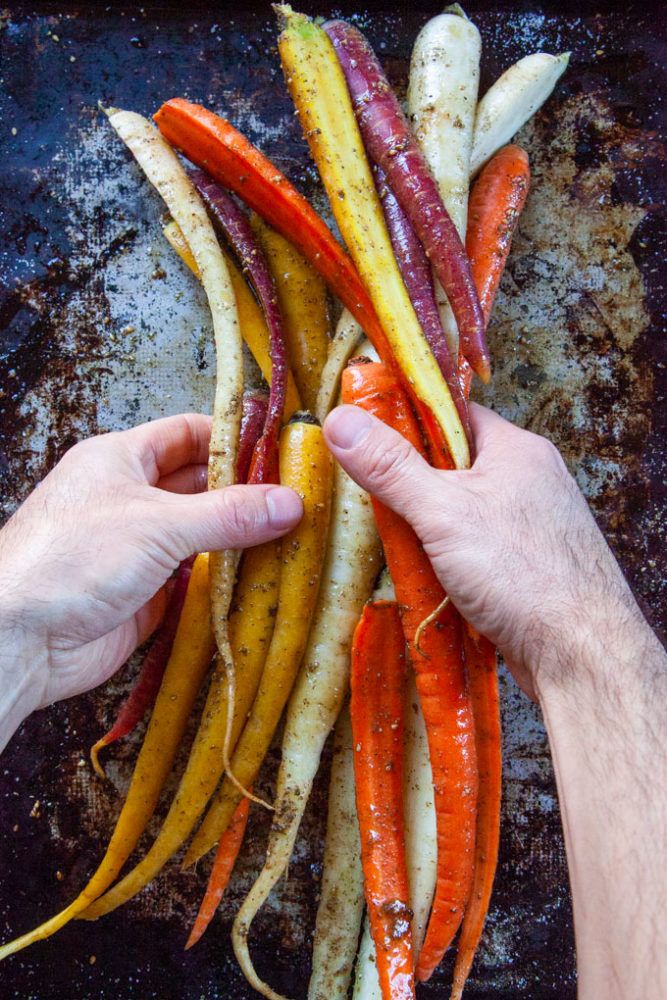 Hands tossing carrots with olive oil and spices.