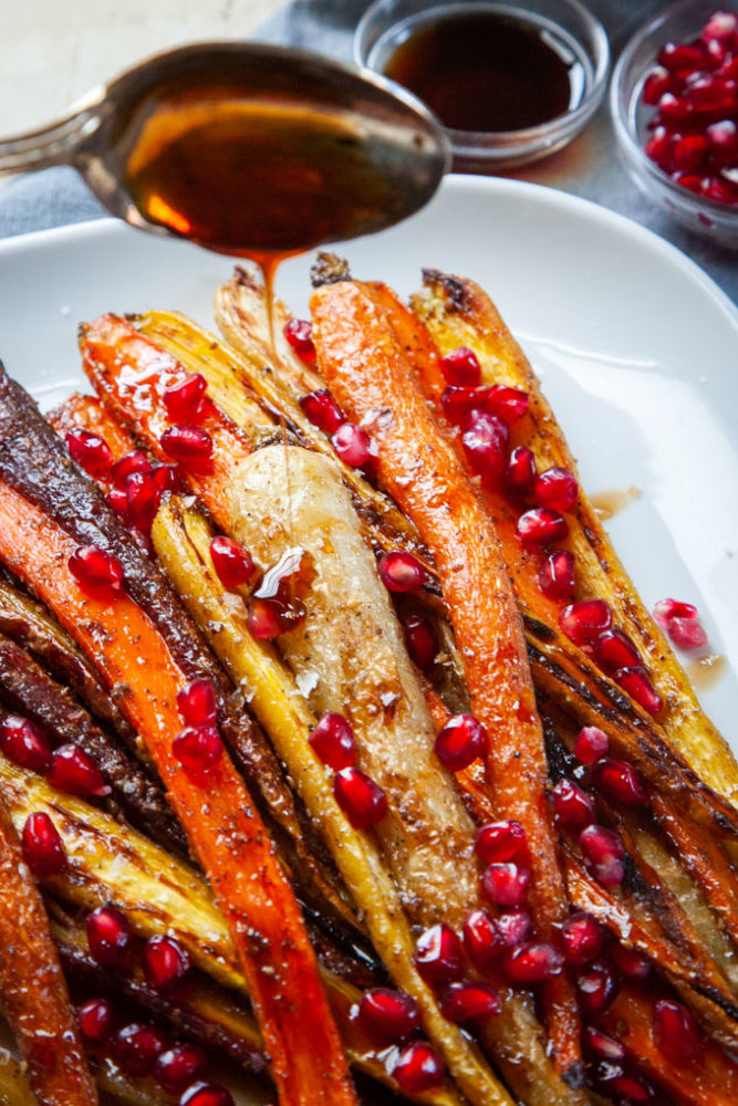 A spoon drizzling pomegranate molasses over roasted carrots.